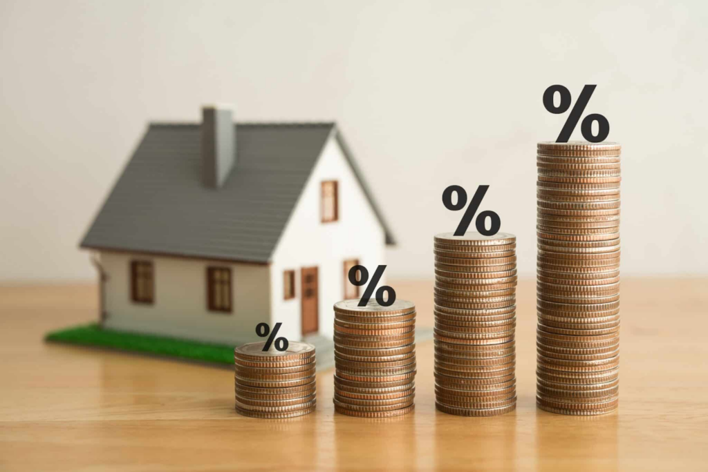 Small play-sized house with coins and percentage signs next to it stacked up inferring various home loan rates signifying the VA Home Loans options.