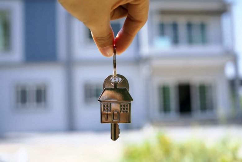 Silver keys with home keychain in front of new home