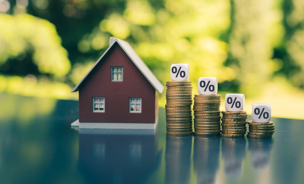 Image of a house with coins and percentages, illustrating the financial impact and importance of understanding mortgage rates and down payments when purchasing a home.